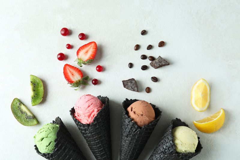 Black cones with ice cream and ingredients on white textured bac