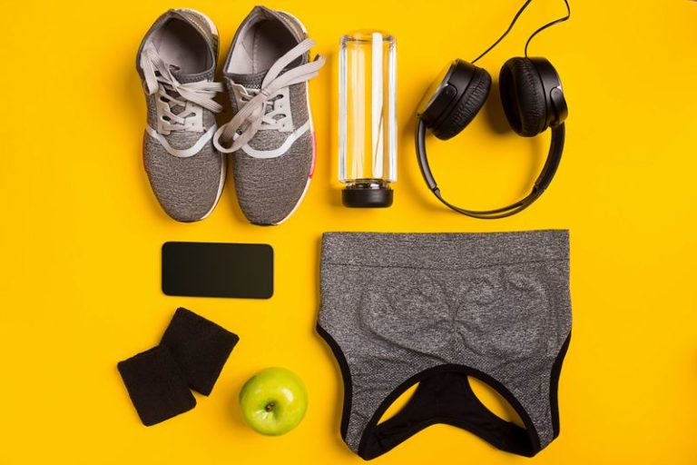 Fitness accessories on yellow background. Sneakers, bottle of water, headphones and sport top